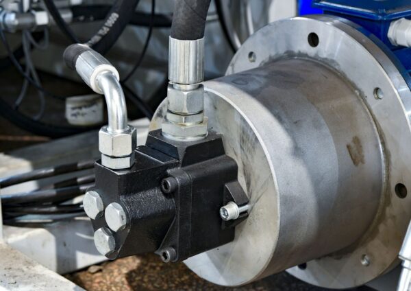 A close-up of a hydraulic pump connected to a motor, showing metal fittings and high-pressure hoses.