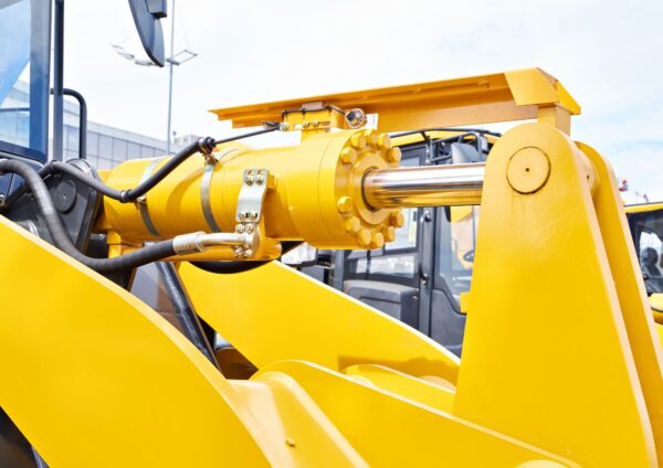 Close-up of a yellow hydraulic cylinder on heavy machinery with visible hydraulic components and connections.