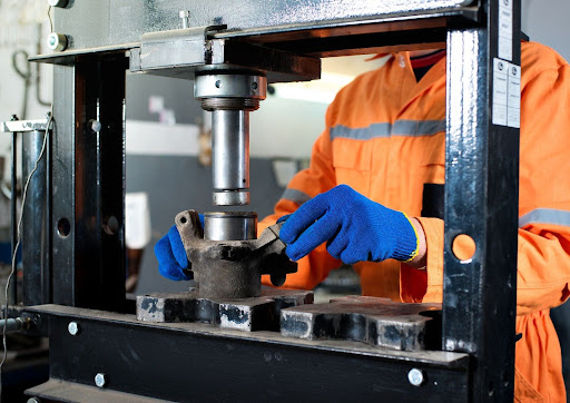 A worker in safety gear operates a hydraulic press to repair a metal component with precision machining.